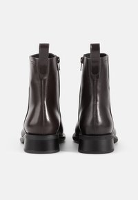Brown leather ankle boots with a glossy finish, side zippers, and looped pull tabs; flat soles with a slightly elevated heel.