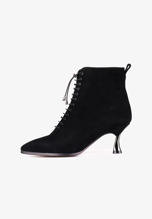 Sorte ruskindsankelstøvler med spids tå, snørelukning og metallisk kitten heel. Har en lille løkke bagpå for nem påtagning.