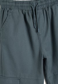 Pantalones de color verde oscuro con cintura elástica y cierre con cordón, bolsillos laterales y una textura de tejido suave. Presenta detalles de costura a medida.