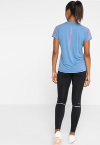 Camiseta deportiva azul claro de manga corta, con detalles rosas en los hombros; leggings negros con detalles reflectantes y ajuste ceñido.