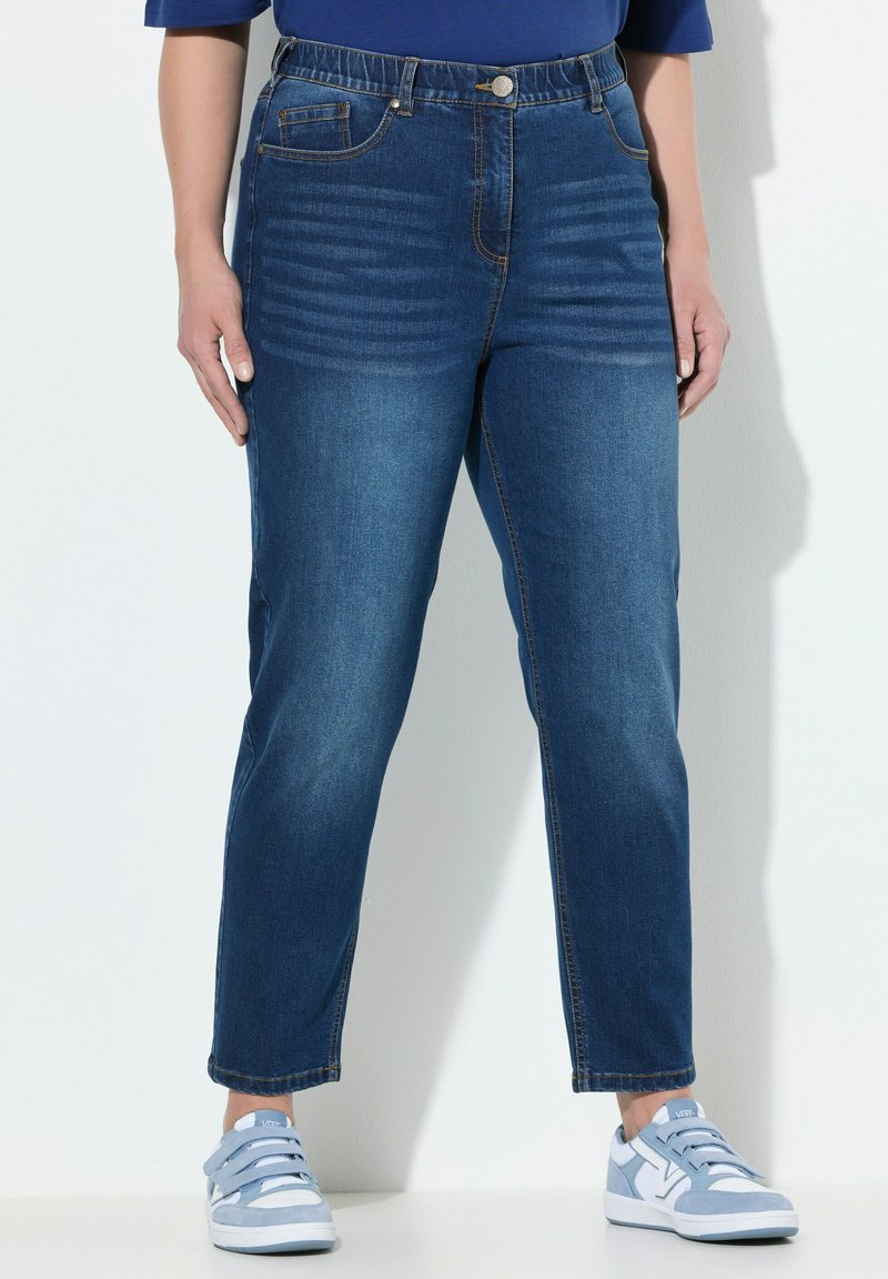 Vaqueros de mezclilla azul de cintura alta con corte recto, que cuentan con bolsillos delanteros, líneas verticales sutiles y dobladillos remangados. Combinados con zapatillas de deporte azul claro.