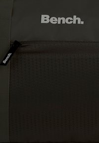 Donkergrijze rugzak van gestructureerde stof met een hexagonaal patroon. Witte "Bench."-logo aan de voorkant en een zijritsdetail.