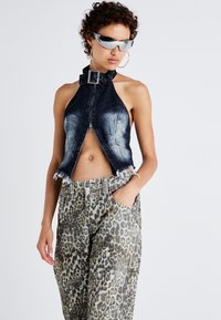 Haut en jean cropped à halter avec fermeture éclair à l'avant, couleur bleu délavé et bords bruts, associé à un pantalon taille haute à imprimé léopard. Lunettes de soleil argentées portées.
