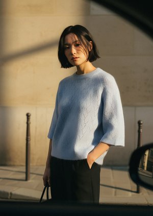 Hellblauer gestrickter Pullover mit Rautenmuster, kurzen Ärmeln und lockerer Passform, kombiniert mit dunklen Hosen. Weicher Stoff und lässiges Design.