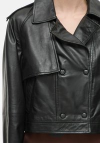 Juodas odinis trumpas švarkas su dvigubos sagos dizainu, plačiais atlapais ir dviem ryškiais mygtukais priekyje, turintis lygų paviršių.