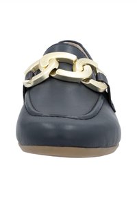 Mocassin en cuir noir avec une grande chaîne décorative en or sur le dessus et une semelle marron clair, vu de face.