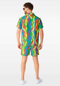 Bunt gemustertes Kurzarmhemd und Shorts-Set. Hergestellt aus leichtem Stoff mit einem lebendigen Wellenmuster in Rot, Grün, Blau und Gelb. Weiße Sneakers.