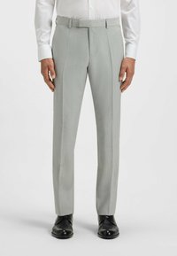 Jasnoszare spodnie garniturowe o dopasowanym kroju, teksturowany materiał, gładki przód i subtelne zagniecenia, w połączeniu z ciemnymi butami.