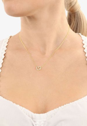 Collar de oro con un pequeño colgante circular hecho de piezas unidas adornado con pequeños diamantes, llevado por una mujer que viste una blusa blanca.
