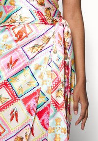 Gros plan d'une robe portefeuille nouée avec des motifs patchwork colorés comprenant des piments, des coquillages, des bananes et des animaux sur un fond clair.
