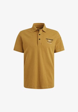 Polo shirt jaune moutarde en coton avec un plastron à trois boutons. Doté d'un texte imprimé en noir sur la poitrine et d'une poche sur la manche gauche.