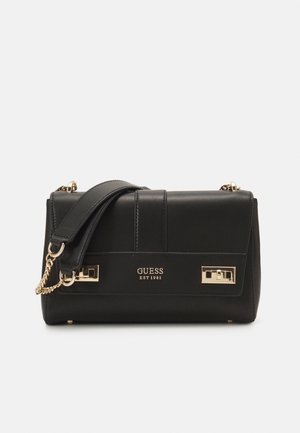 Schwarze Guess Schultertasche mit goldener Kette und Schnallendetails, gepolstertem Riemen und Logo „GUESS EST 1981“ auf der Vorderklappe.