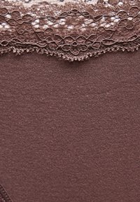 Κοντινό πλάνο μωβ ύφασματος με περίτεχνη δαντέλα που διαθέτει λουλουδάτα και κυκλικά σχέδια κατά μήκος της επάνω άκρης.