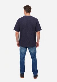 Navy short-sleeve shirt with a geometric pattern, paired with light blue jeans and dark shoes. The shirt features a round neckline and a relaxed fit.