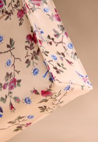 Blomstret mulepose i beige stof med mønster af røde og blå blomster samt grønne blade, med en struktureret form og sømme ved kanterne.