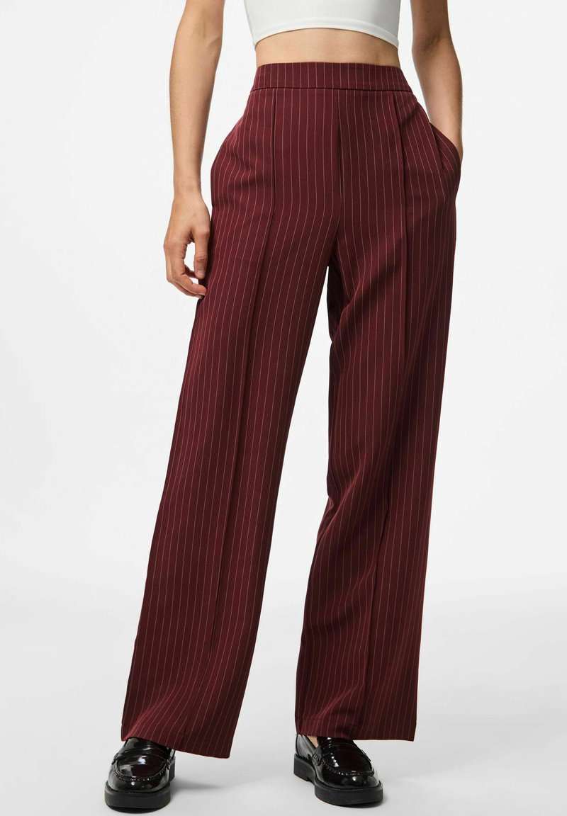 Pantalons larges bordeaux avec des rayures blanches verticales, dotés d'une taille haute et de poches latérales, associés à des mocassins noirs brillants.