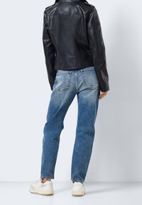 Czarna skórzana kurtka motocyklowa, przetarte niebieskie dżinsy, białe trampki; widoczne tylne kieszenie i efekt gradientu na dżinsach.