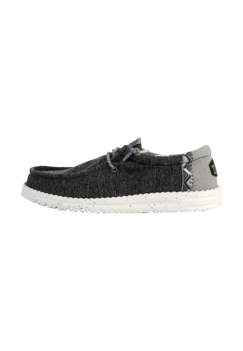 Zapato slip-on de tela gris con punta redondeada, que presenta una suela moteada blanca y acentos estampados en el talón.