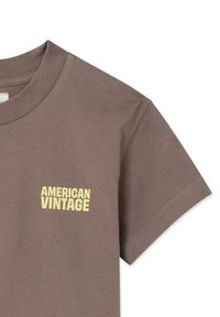 T-shirt di cotone marrone a maniche corte, con logo giallo "AMERICAN VINTAGE" sul petto. Texture liscia e vestibilità regolare.