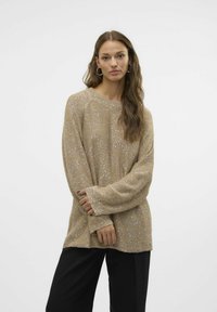 Strikket trøje i beige med subtile glimmer, har en rund halsudskæring og lange ærmer, parret med sorte bukser. Blød tekstur og afslappet pasform.