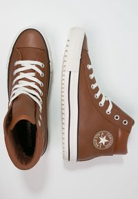 Brown leather high-top sneakers with white laces, rubber sole, and signature Converse star logo on the side. Textured upper and smooth finish.