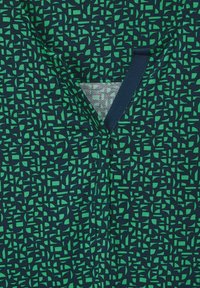 Bavlněná košile s námořnickým pozadím, na kterém je geometrický zelený vzor. Obsahuje výstřih do V a texturované detaily.