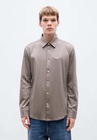 Μακ ρυμάνικο, πουκάμισο με γιακά σε απαλό μπεζ ύφασμα, με μπροστινή σειρά κουμπιών, διακριτική κέντημα λογοτύπου και καμπύλη γραμμή στη βάση.