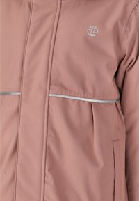 Ljusrosa jacka i slät tyg, med en reflekterande silverrand, en logo och en framficka. Ren design med moderna linjer.