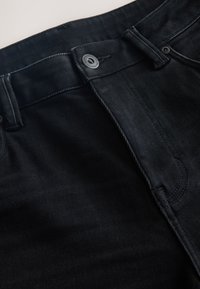 Nahaufnahme des Bundes einer schwarzen Denim-Jeans mit Knopfverschluss, Gürtelschlaufen und sichtbaren Nähten.