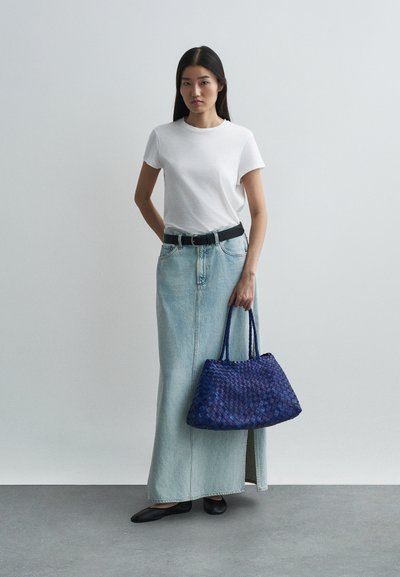 Λευκό κοντομάνικο t-shirt, γυαλιστερή ψηλόμεση φούστα τζην σε φωτεινό χρώμα, μαύρη ζώνη και μεγάλη πλεκτή μπλε τσάντα. Λείο ύφασμα, χαλαρή εφαρμογή.