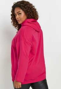 Sudadera fucsia con bolsillo canguro, capucha con cordón y puños acanalados, combinada con leggings sintéticos negros. Tejido suave de mezcla de algodón.