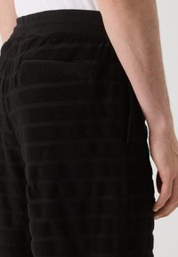 Zwart gestreepte sweatpants van een textuurstof. Voorzien van een elastische tailleband en een zijzak, met een gestreept patroon door het hele stuk.