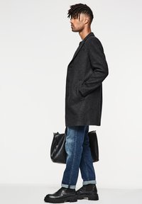 Abrigo de lana negro, de botonadura sencilla, con solapas con muesca. Combinado con vaqueros de mezclilla azules y botas de cuero negras hasta el tobillo. Lleva un bolso negro.