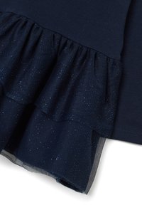 Dunkelblauer Stoff mit geschichteten, glitzernden Tüllrüscheln am Rand, die Struktur und Glitzerdetails auf einem Kleidungsstück zeigen.