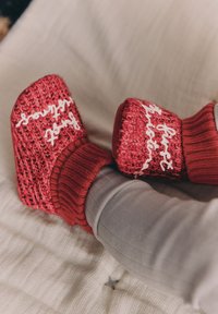 Czerwone, dziergane buciki z teksturowanym wzorem i białym napisem. Posiadają prążkowany mankiet na kostkę oraz kwadratowy kształt palców.