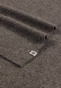 Brauner Filzstoff aus Wolle mit weicher Textur, verfügt über umgeschlagene Kanten und ein Etikett mit einem Logo in einer Ecke. Die Oberfläche ist flauschig und gleichmäßig.