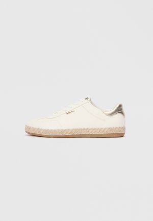 White canvas sneaker with a textured surface, metallic gold accent on the heel, and a jute-woven midsole. Features lace-up design.