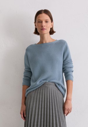 Jasnoniebieski sweter dzianinowy z dekoltem w łódkę i podwiniętymi rękawami, w połączeniu z szaro-plisowaną spódnicą midi, na neutralnym tle.