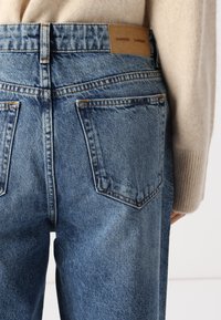 Light blue denim jeans with a high waist, featuring back pockets, subtle fading, and a leather brand tag stitched at the back waistband.