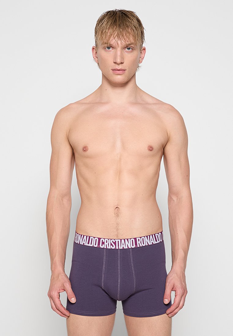Boxers morados con una cinturilla blanca de marca que presenta "Cristiano Ronaldo". Textura suave, diseño ajustado y longitud hasta medio muslo.