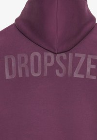 Violetinė gobtuvinė palaidinė su didelėmis ryškiomis raidėmis "DROPSIZE" nugaros pusėje. Minkšta, tekstūruota medžiaga su laisvu siluetu.
