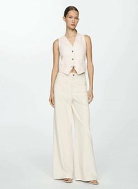 Gilet court beige clair avec un décolleté en V et des boutons, associé à un pantalon crème à jambes larges. Texture lisse, design minimaliste.