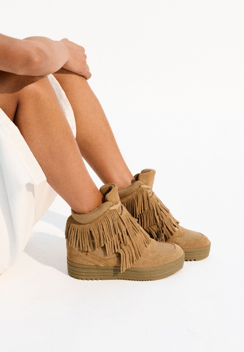 Tan suède high-top sneakers met franjes. Dikke rubberen zool, afgeronde neus en een strikaccent aan de bovenkant.