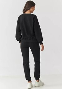 Czarny sweatshirt i dopasowane dresy wykonane z miękkiego materiału, charakteryzujące się luźnym krojem i ściągaczami, noszone z białymi trampkami.