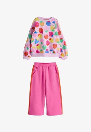 Sweater met lange mouwen met kleurrijke aardbeienprint gecombineerd met roze wijd uitlopende broek met oranje strepen aan de zijkant en een elastische tailleband.