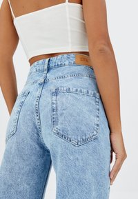 Jeans de tiro alto de color azul claro, fabricados en denim, con un parche de cuero que lleva el logo "STR" y dos bolsillos traseros de forma clásica.