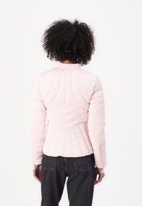 Light pink quilted jacket with a high collar, fitted design, and unique stitching patterns on the back. Features long sleeves and elastic cuffs.