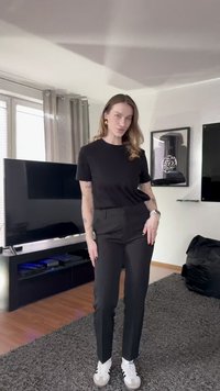 Czarny t-shirt z krótkim rękawem w połączeniu z dopasowanymi czarnymi spodniami i białymi trampkami. Strój cechuje się prostym wzornictwem i luźnym krojem.