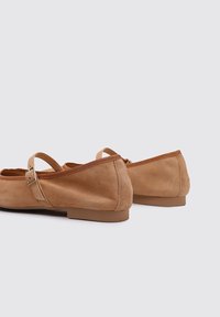 Ballerines en suede beige avec un bout arrondi, une sangle ajustable et une petite semelle en caoutchouc plate. Texture lisse avec un design simple.