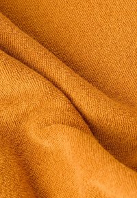 Zbliżenie na pomarańczową tkaninę frotte złożoną, ukazujące pętelkową fakturę oraz miękki, chłonny materiał.